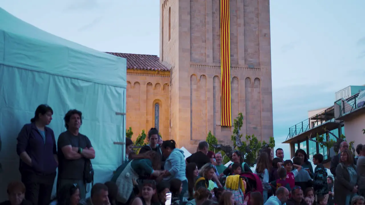 The bell tower of a church with the Senyera the flag of Catalonia hanging from the top of the bell tower falling onto a square full of people on Saint George's Day Sant Jordi