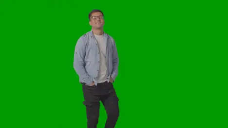 Three Quarter Length Portrait Of Casually Dressed Smiling Young Man Wearing Glasses Against Green Screen 