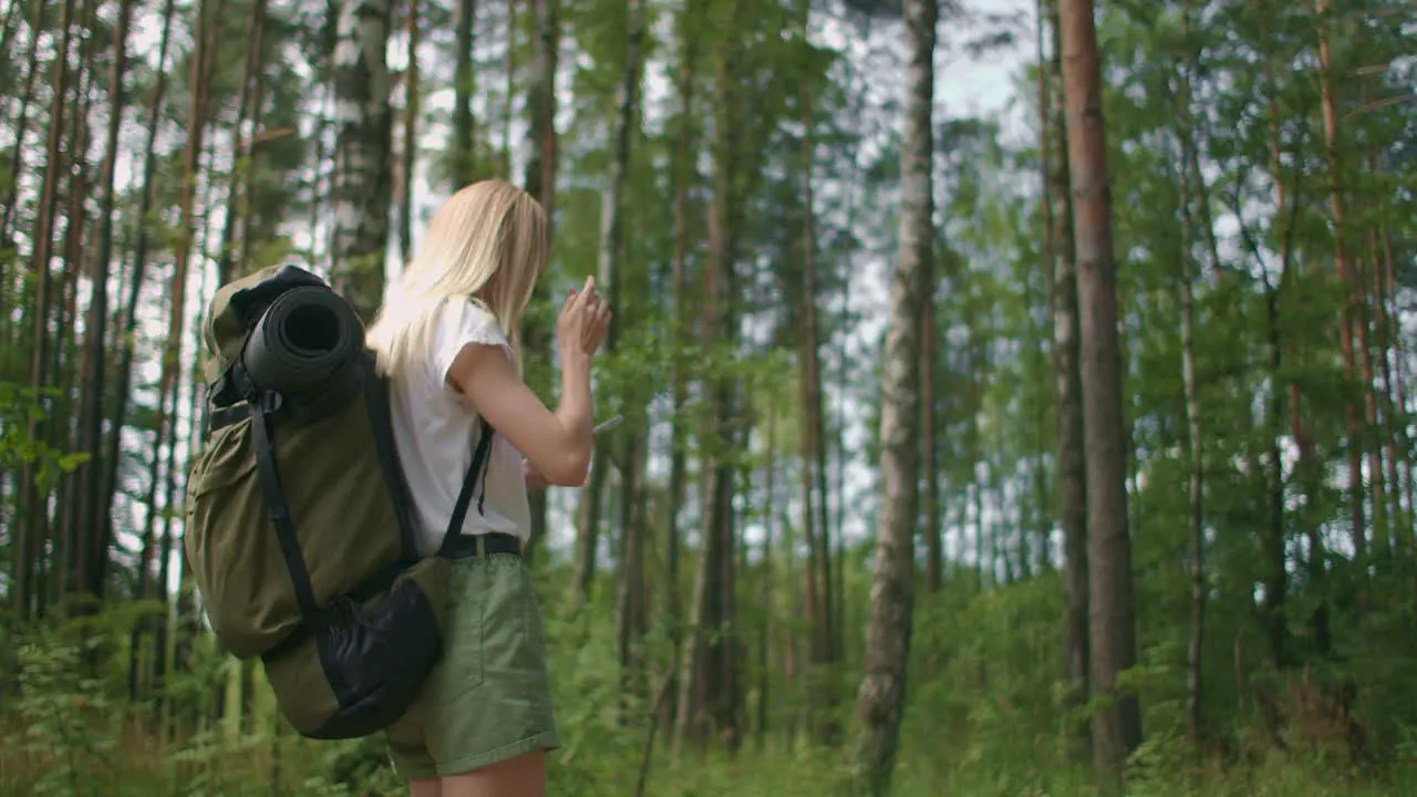 A young woman with a mobile phone walks through the forest traveling with a backpack in slow motion Traveler in shorts in the woods looking for gps satellites