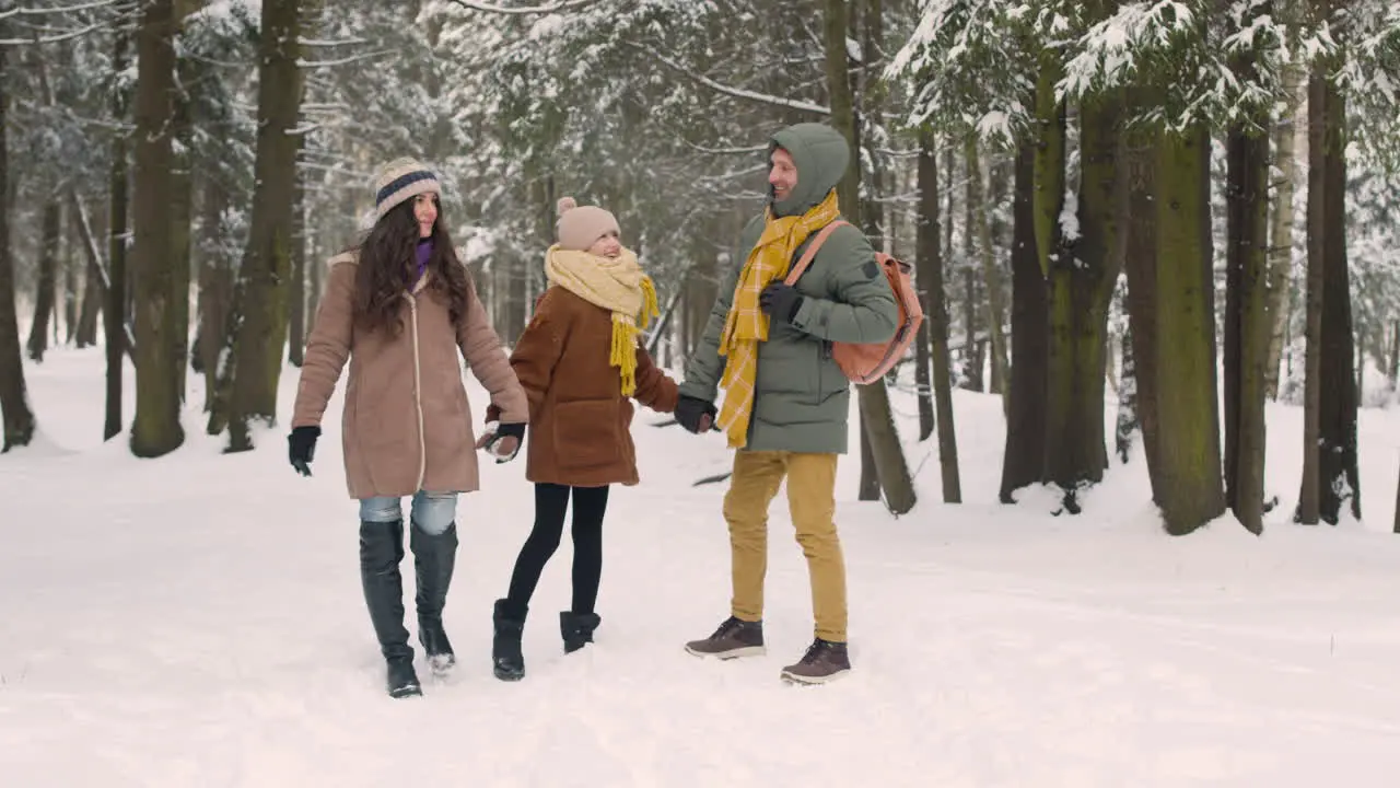 Front View Of Parents And Daughter Dressed In Winter Clothes In Snowy Forest