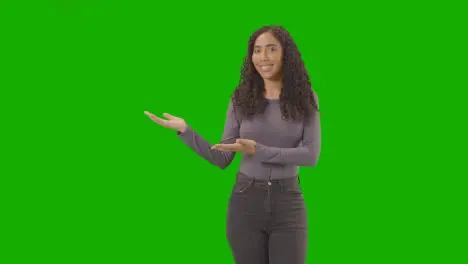 Portrait Of Woman Presenting Or Demonstrating Item Against Green Screen Smiling At Camera 2