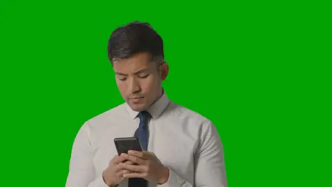 Studio Shot Of Serious Businessman In Shirt And Tie Using Mobile Phone Against Green Screen 