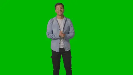 Portrait Of Casually Dressed Smiling Young Man With Arms Outstretched In Welcome Against Green Screen 