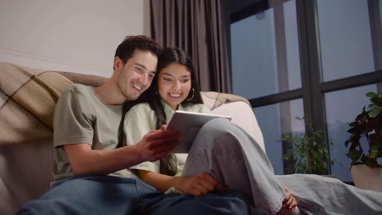 Vista Inferior De Una Pareja Viendo Una Película Cómica En Una Tableta Mientras Se Sienta En El Suelo En Casa 1