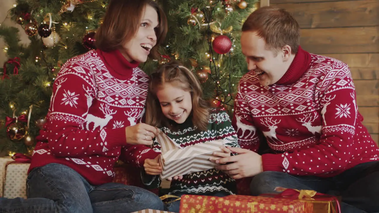 Glückliches Kleines Mädchen Das Geschenk Auspackt Während Es Mit Seiner Mutter Und Seinem Vater Vor Dem Weihnachtsbaum Zu Hause Sitzt 1