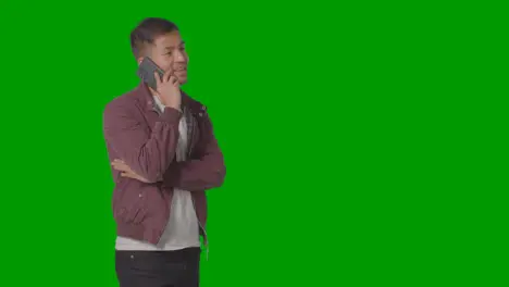 Studio Shot Of Smiling Casually Dressed Young Man Talking On Mobile Phone Against Green Screen 