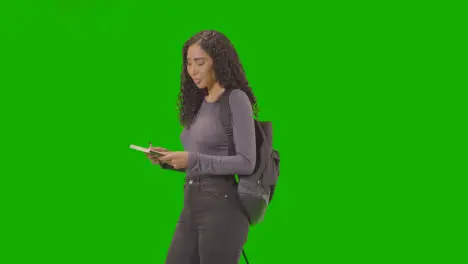 Portrait Of Female College Or University Student With Backpack And Notebook Against Green Screen Smiling At Camera