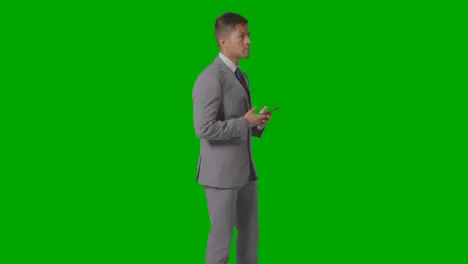 Three Quarter Length Studio Shot Of Businessman In Suit Looking At Mobile Phone Against Green Screen 3