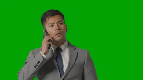 Studio Shot Of Serious Businessman In Suit Taking Call On Mobile Phone Against Green Screen 