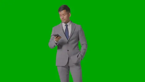 Three Quarter Length Studio Shot Of Businessman In Suit Talking On Mobile Phone Against Green Screen 