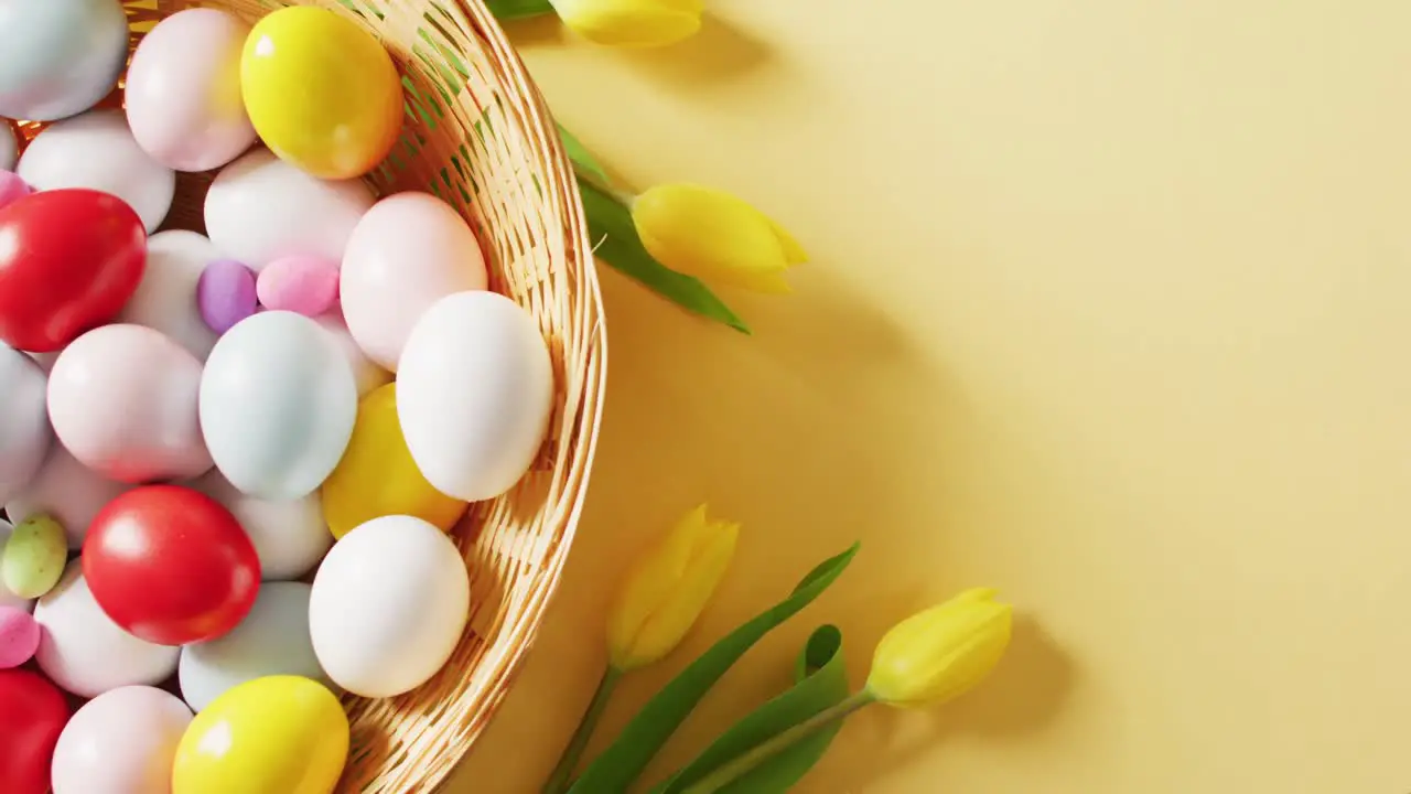 Basket with colorful easter eggs and tulips on yellow background with copy space