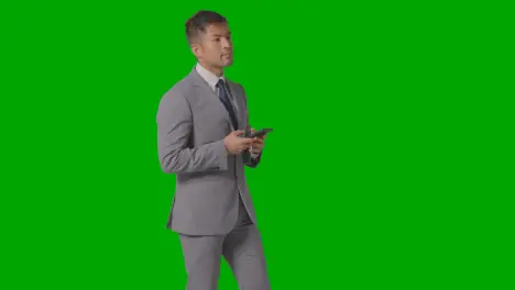 Three Quarter Length Studio Shot Of Businessman In Suit Looking At Mobile Phone Against Green Screen 1