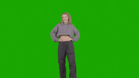 Full Length Studio Portrait Of Smiling Young Woman Against Green Screen