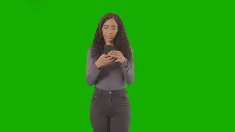 Three Quarter Length Portrait Of Woman Text Messaging On Mobile Phone Against Green Screen