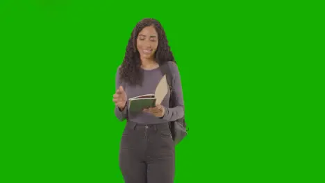 Portrait Of Female College Or University Student Writing In Notebook Against Green Screen Smiling At Camera