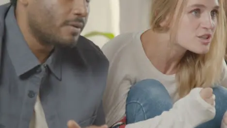 Multi-Cultural Friends Celebrating Watching Sports Game On TV Sitting On Sofa At Home Together