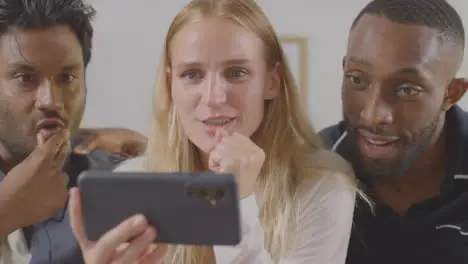 Multi-Cultural Friends Celebrating Watching Sports Game On Mobile Phone Sitting On Sofa At Home Together 3