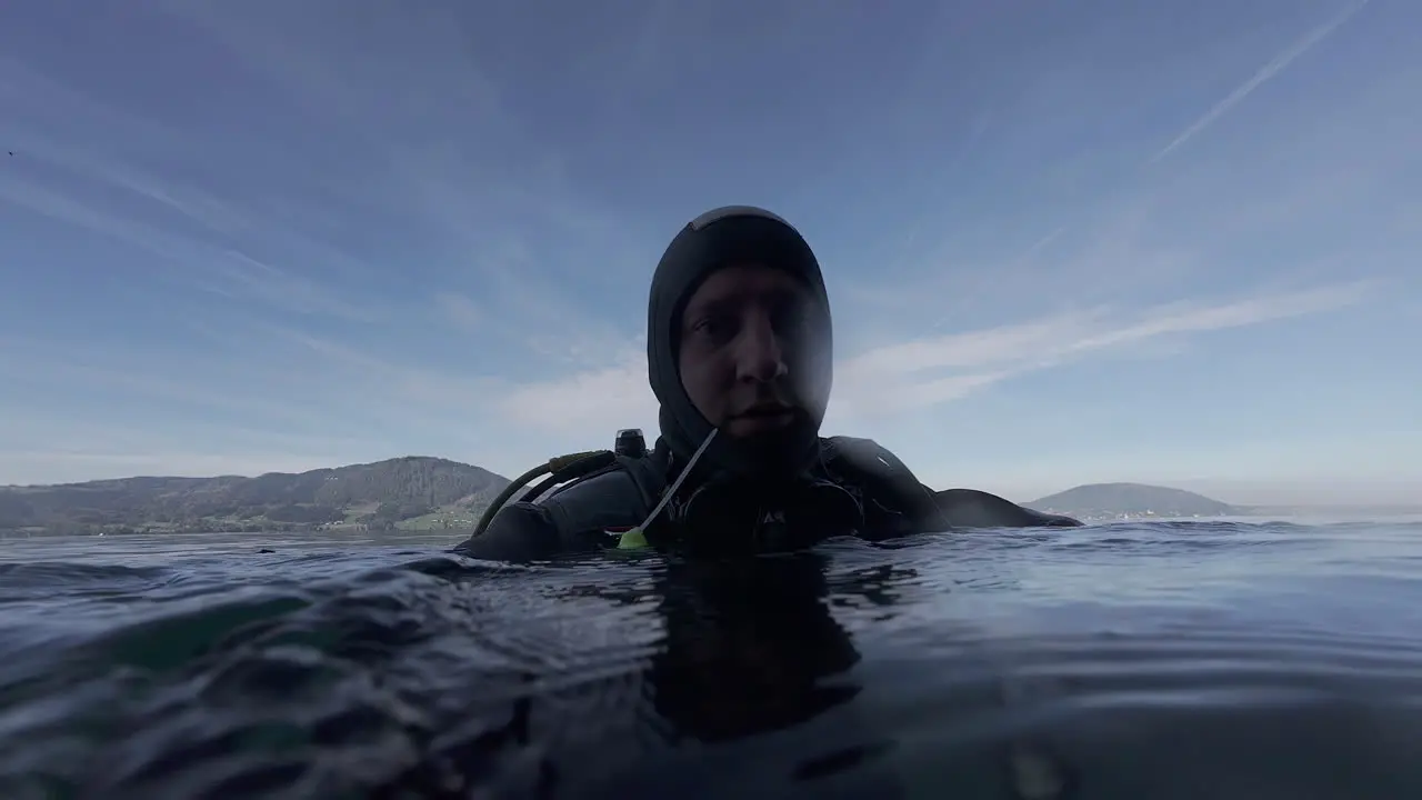 Scuba diver in wetsuit without mask looking around above shore water