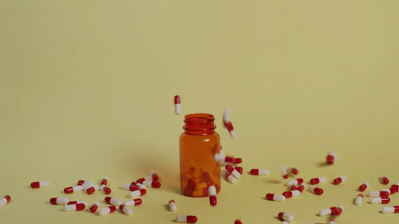 Slow motion wide shot as a handful of pills fall towards an open pill bottle