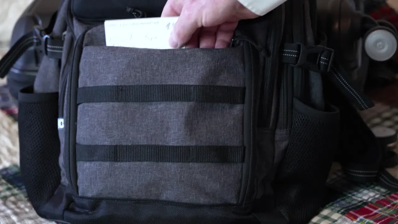 Man's hand seen putting his COVID vaccination card in use travel carry on bag for a trip close up