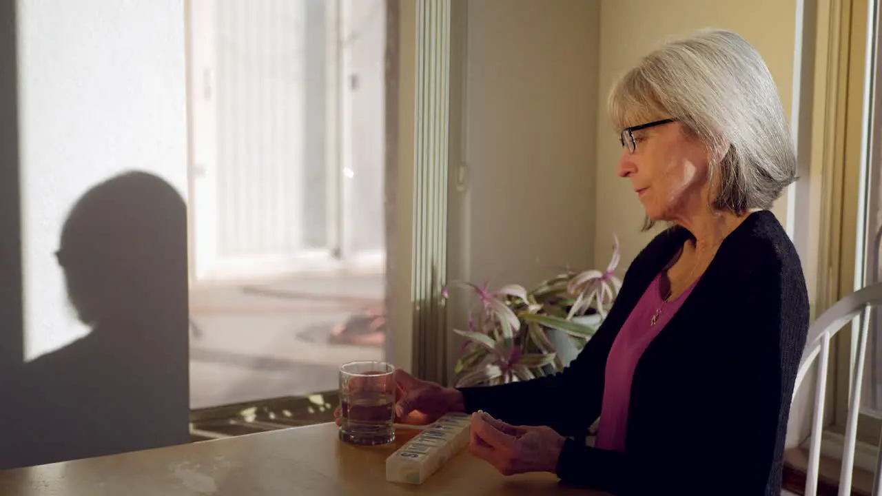 An elderly woman taking her daily prescription medication and vitamin pills with a glass of water then smiling with good health