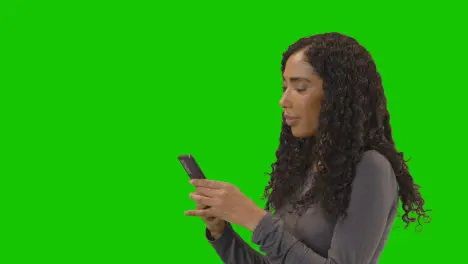 Profile Shot Of Woman Text Messaging On Mobile Phone Against Green Screen