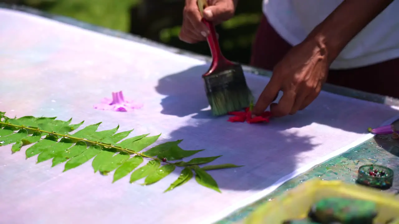 teaching homemade batik sarong pareo Dark skin man wetting hibiscus flower on white cloth Mahe Seychelles 25fps 2