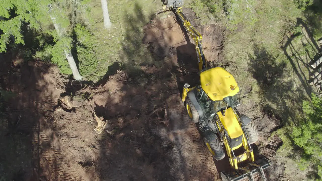 JCB tractor working in forest taking out tree roots drone shot from above doing half circle around tractor