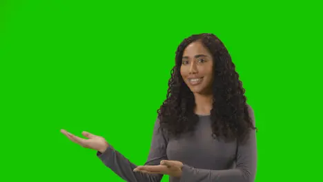 Portrait Of Woman Presenting Or Demonstrating Item Against Green Screen Smiling At Camera