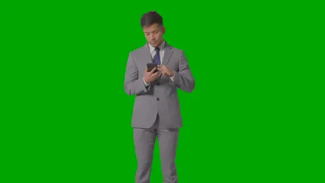 Three Quarter Length Studio Shot Of Businessman In Suit Looking At Mobile Phone Against Green Screen 4