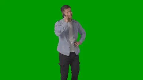 Studio Shot Of Casually Dressed Smiling Young Man Talking On Mobile Phone Against Green Screen 