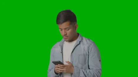 Studio Shot Of Casually Dressed Young Man Messaging On Mobile Phone Against Green Screen 1