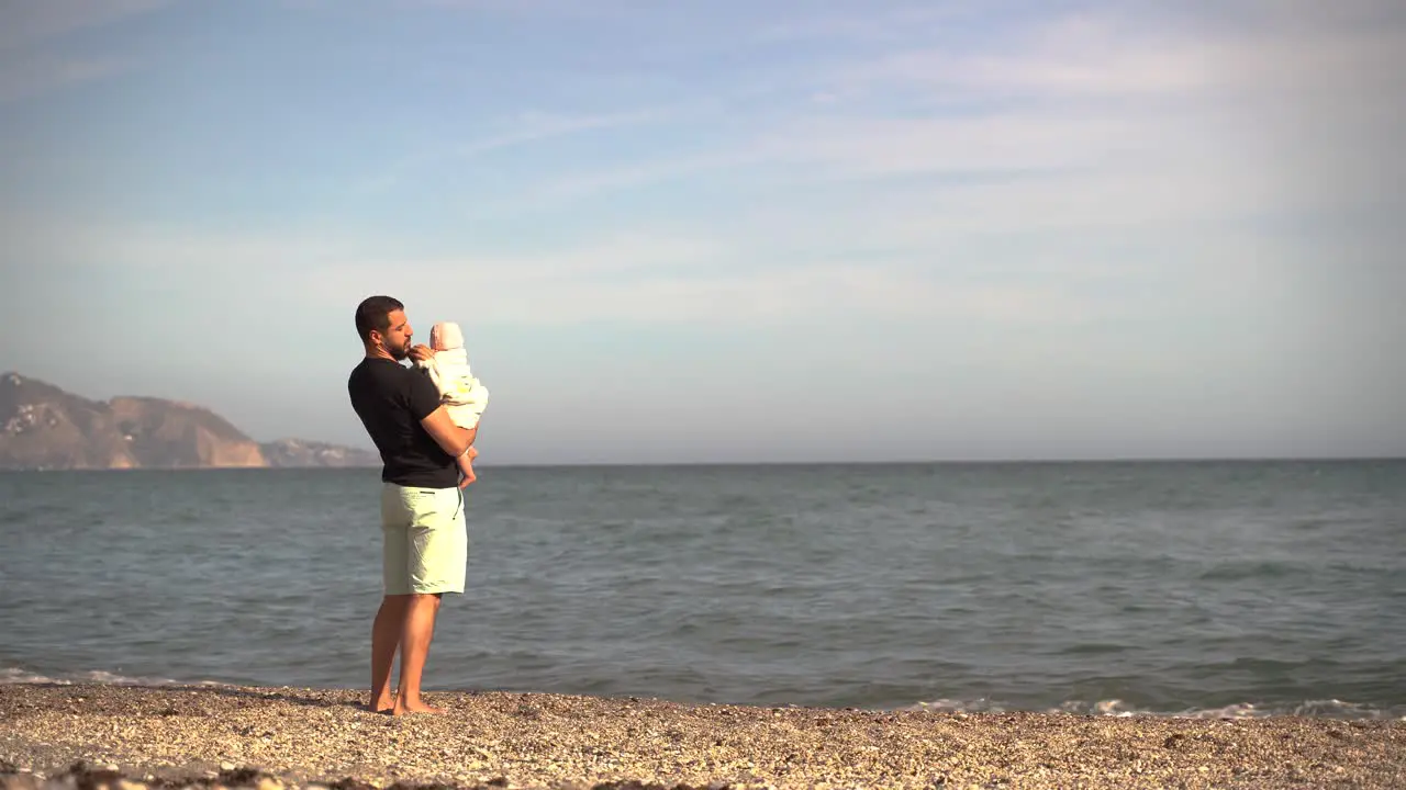 Father lovingly holding small baby while looking out on the ocean at beach