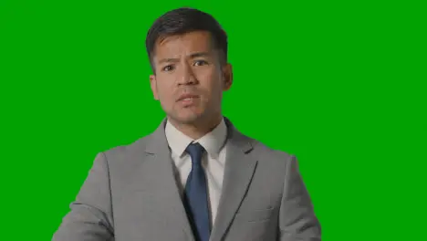 Portrait Of Angry Businessman In Suit Against Green Screen Talking To Camera