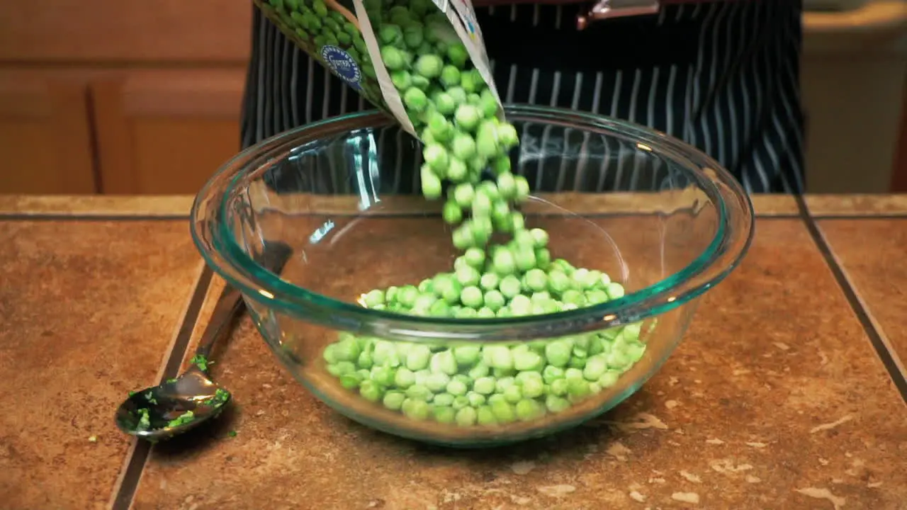 Cook pours frozen peas from plastic packaging into glass bowl slowmo