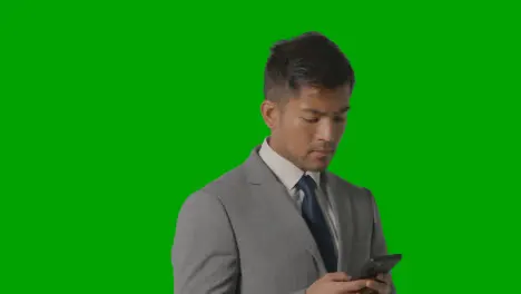 Studio Shot Of Businessman In Suit Against Green Screen Moving And Using Mobile Phone 