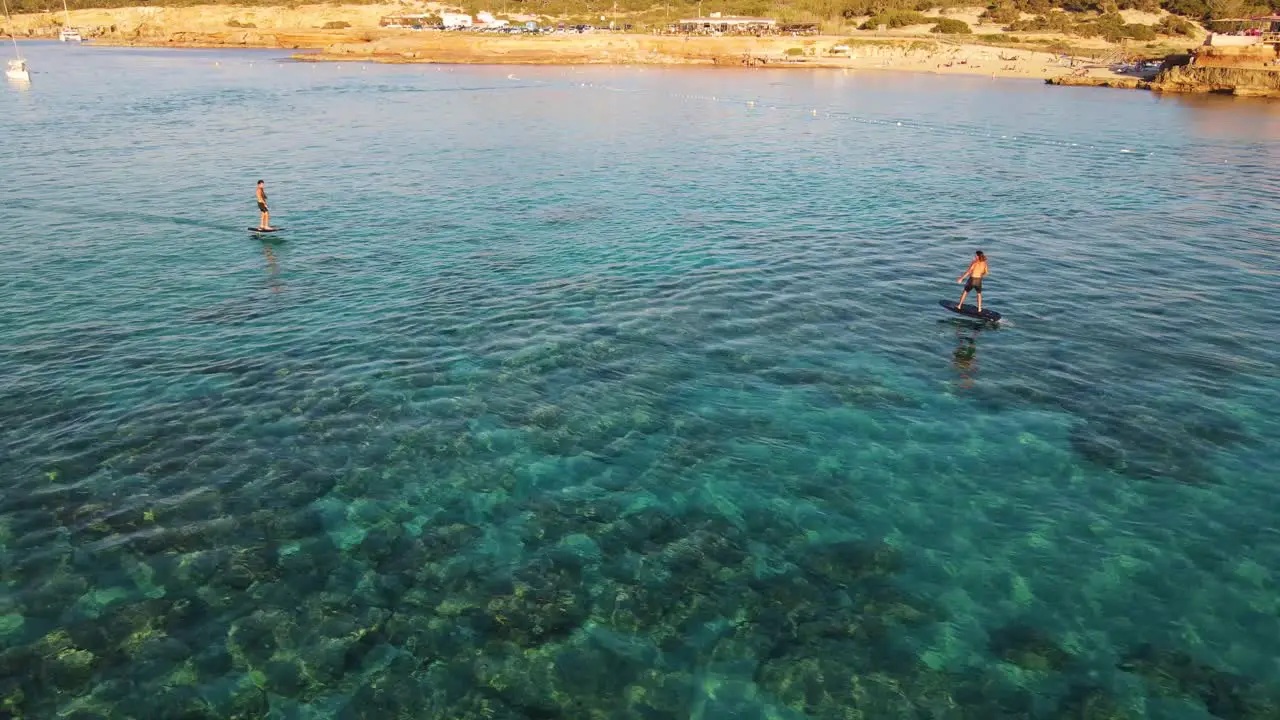 Aerial shot of people surfing with eFoil electric surfboards at Cala Escondida in Ibiza Spain