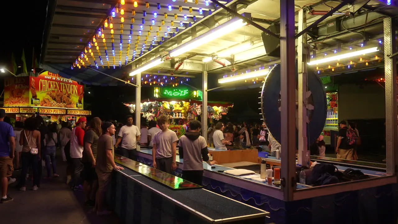 Neon lights flash as people play carnival games on a dark evening at the fair