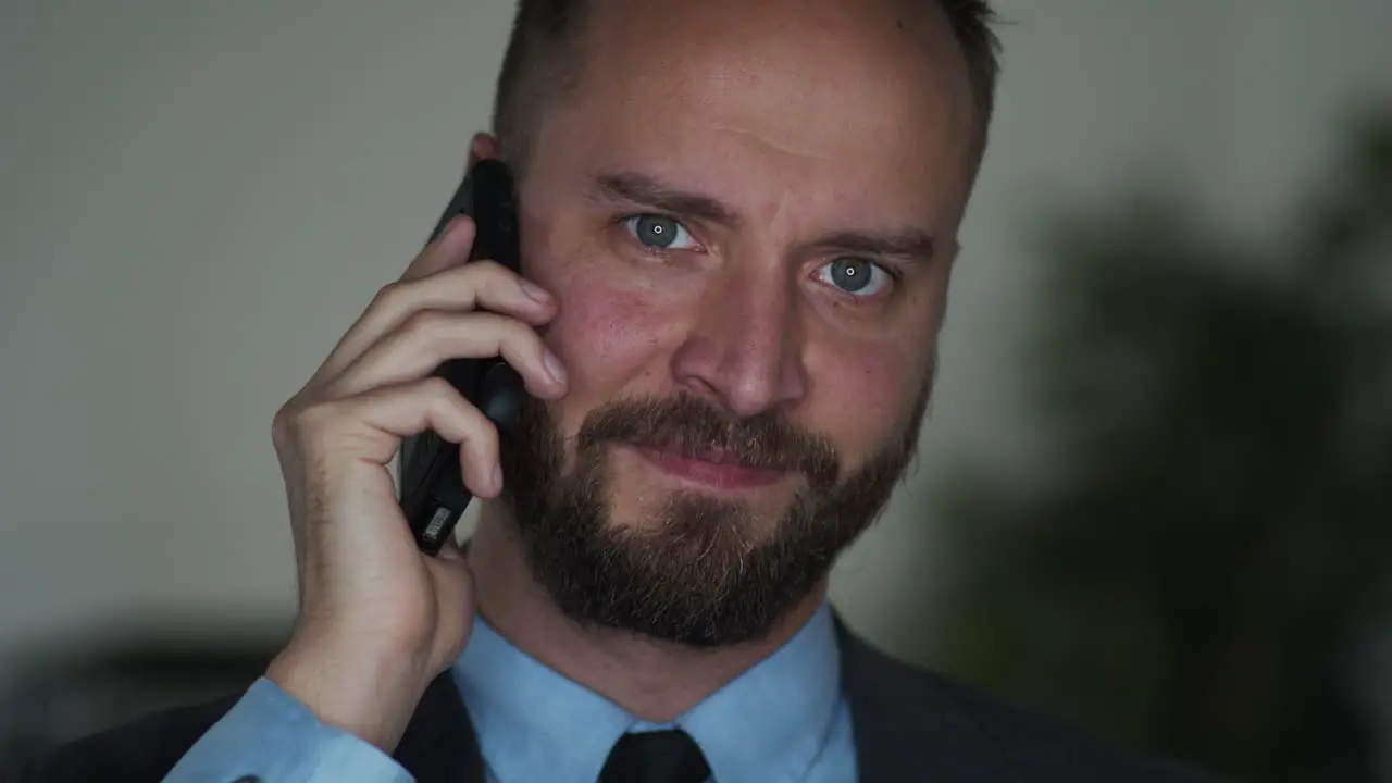 Bearded businessman on cellphone talks and looks in the camera and smiles