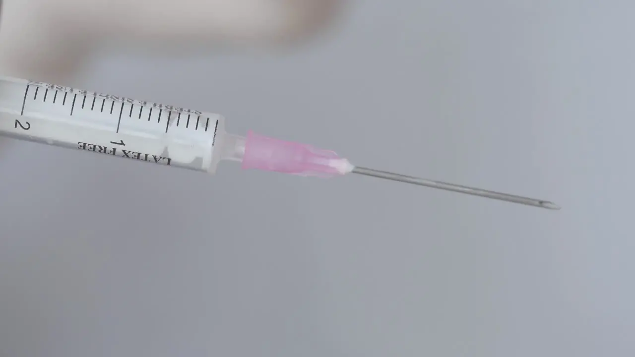 Hand With Disposable Glove Removing Plastic Cap Of Syringe Needle close up