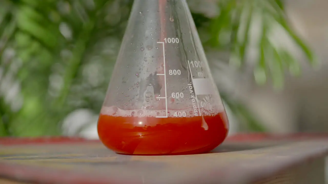 Slow motion colourful measure of red liquid pouring into glass medical flask close up