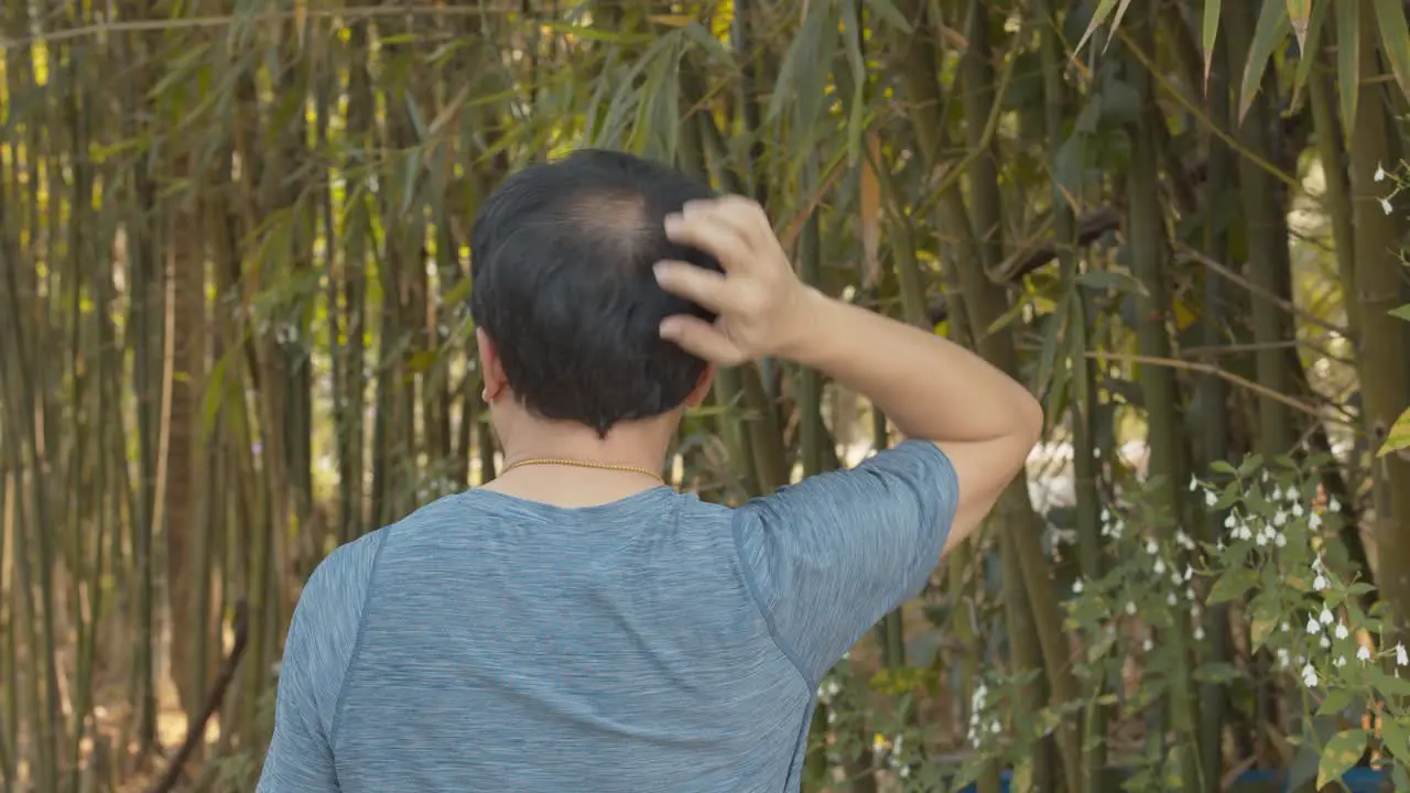 Balding man walking in a bamboo garden can't stop scratching his itchy scalp