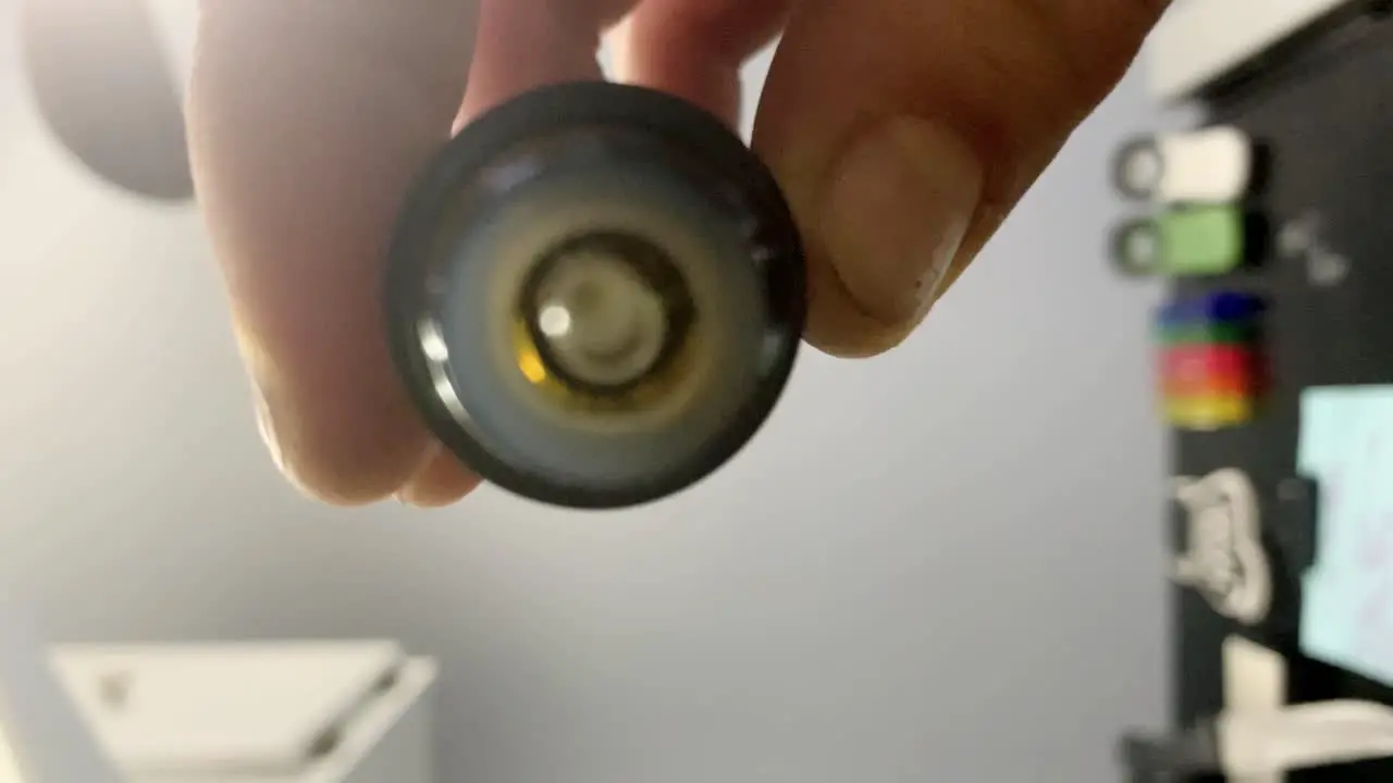 Close-up of clear liquid drops hitting the camera lens as male fingers holding small brown dropper bottle drips