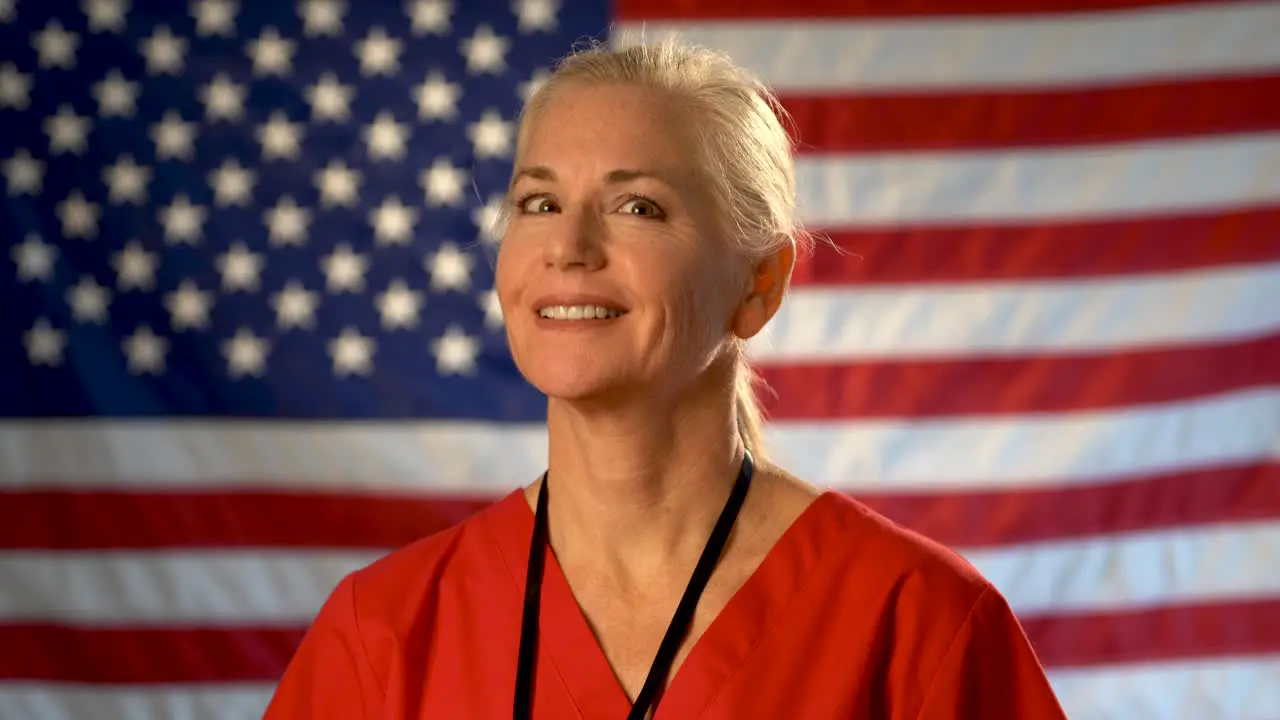 Medium tight portrait of nurse looking to the left and then at camera relieved happy and nodding her head with American flag behind her