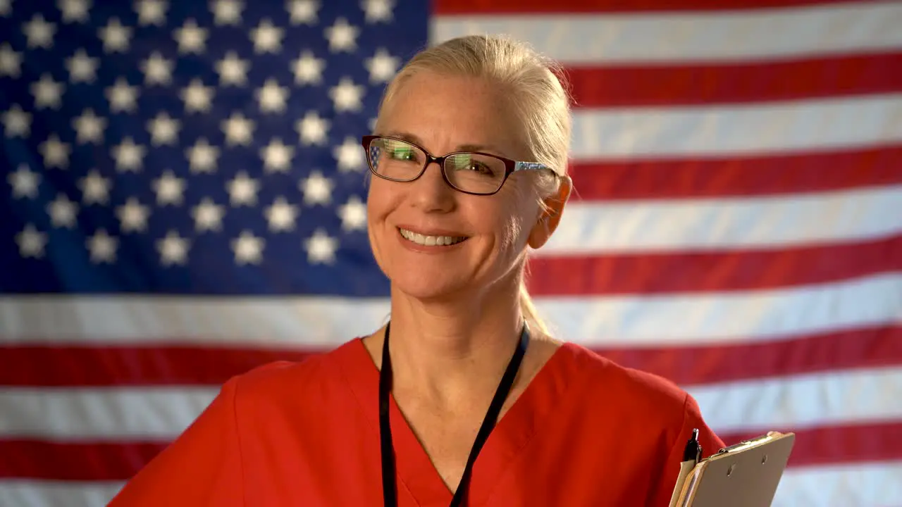 Medium tight portrait of a smiling healthcare nurse with clipboard with out of focus American flag