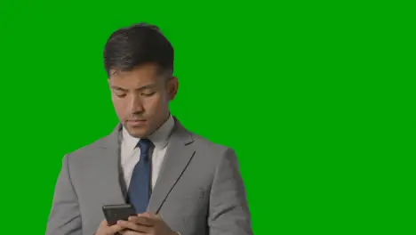 Portrait Of Businessman In Suit Against Green Screen Messaging On Mobile Phone 1