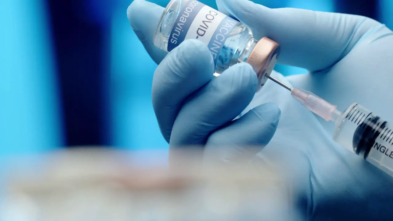 A doctor or nurse wearing latex gloves fills a syringe with the COVID vaccine isolated close up