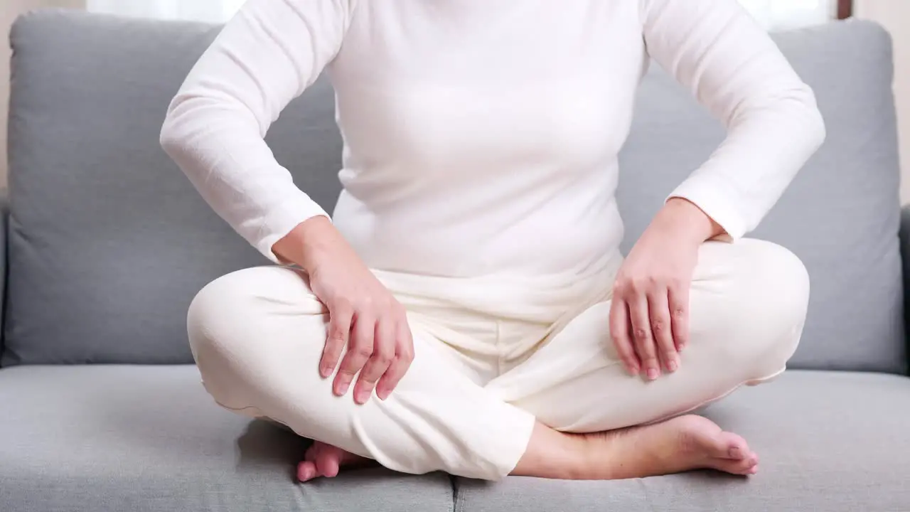 Young woman in cross-legged position on the sofa performing self massage on her legs