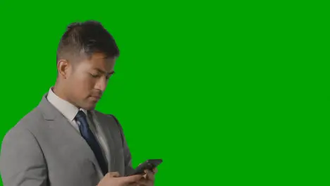 Portrait Of Businessman In Suit Against Green Screen Messaging On Mobile Phone