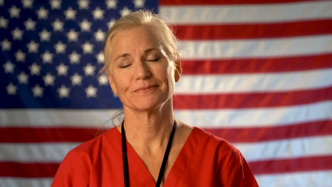 Medium tight portrait of nurse looking relieved happy and nodding her head with American flag behind her